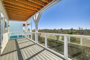 Un terrazza in legno con balaustra in vetro che si affaccia su un paesaggio naturale.