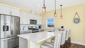 Una cocina moderna con armarios blancos, electrodomésticos de acero inoxidable y una isla central con taburetes de bar.
