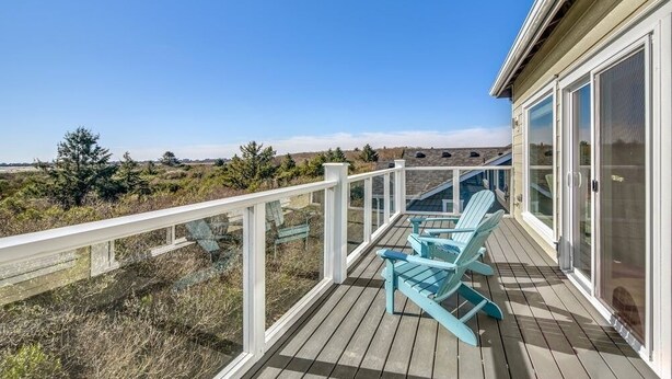 Una terraza de madera con barandilla, dos sillas Adirondack azules y un vidrio que da a un área cubierta.