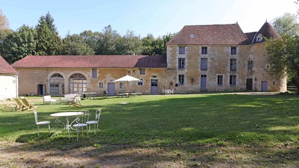 Ein großes Steinhaus mit vielen Fenstern und einem Innenhof mit Außenbestuhlung.