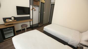 Une chambre d’hôtel avec deux lits simples, un bureau avec une bouilloire, une télévision et une armoire.