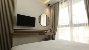 A hotel room with a bed, a mounted TV, a bedside table with a lamp, and a window with curtains. - Moja City Hotel (Istanbul)