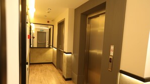 A hallway with wooden flooring, a mirror, and two elevators. - Moja City Hotel (Istanbul)