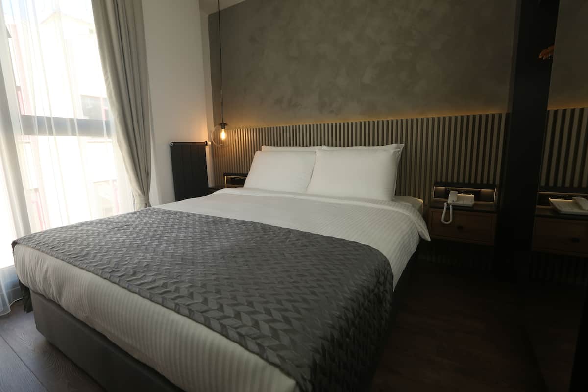 A modern hotel room with a large bed, a bedside telephone, and a nightstand.