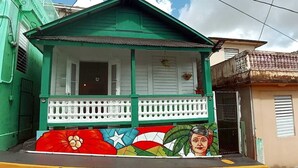 Una casa verde con un porche blanco y un mural colorido en la fachada.