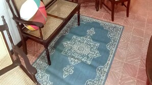 Un comedor con una mesa redonda y sillas de madera, un tapete estampado y una ventana con rejas.