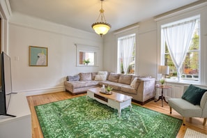 A living room with a sectional sofa, a coffee table, a patterned rug, a television, and a painting of a bird.