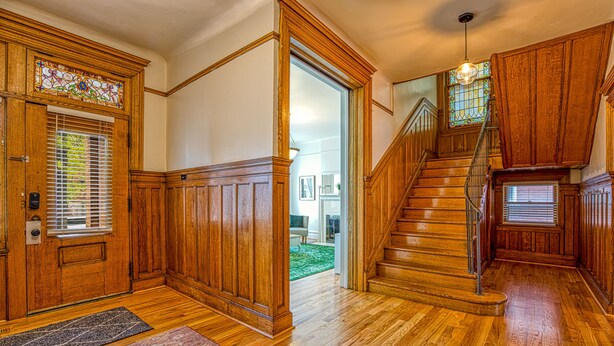 Un escalier en bois avec une rampe, une porte ornée d’un vitrail et un tapis sur le sol.