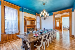 A dining room with a wooden table set for six, white chairs, a chandelier, and a fireplace.
