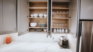 Una cucina con mobili aperti che espongono stoviglie, bicchieri e una macchina da caffè.