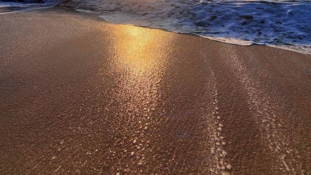 Una spiaggia con un tramonto sull'oceano, le onde che si infrangono sulla riva e un cielo sereno.