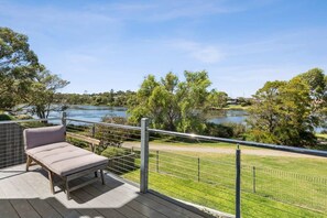 Une terrasse dotée d’un espace salon avec des sièges rembourrés, donnant sur un lac, et entourée d’une clôture en métal et de verdure.