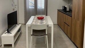 A compact kitchen with a dining area, a TV on a stand, and a modern pendant light.