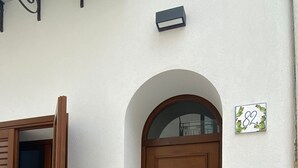 A brown door with a small window above it, a mailbox on the wall, and a house number sign.