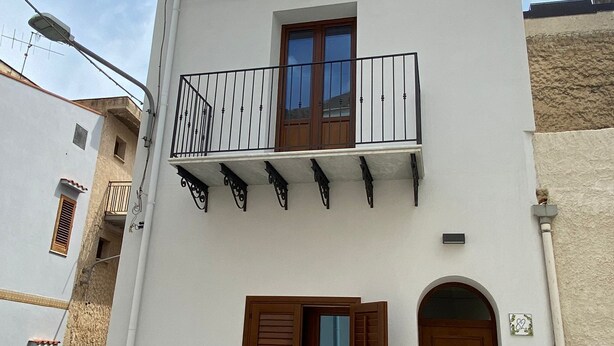 A two-story building with a white facade, wooden shutters, and a balcony with metal railings.