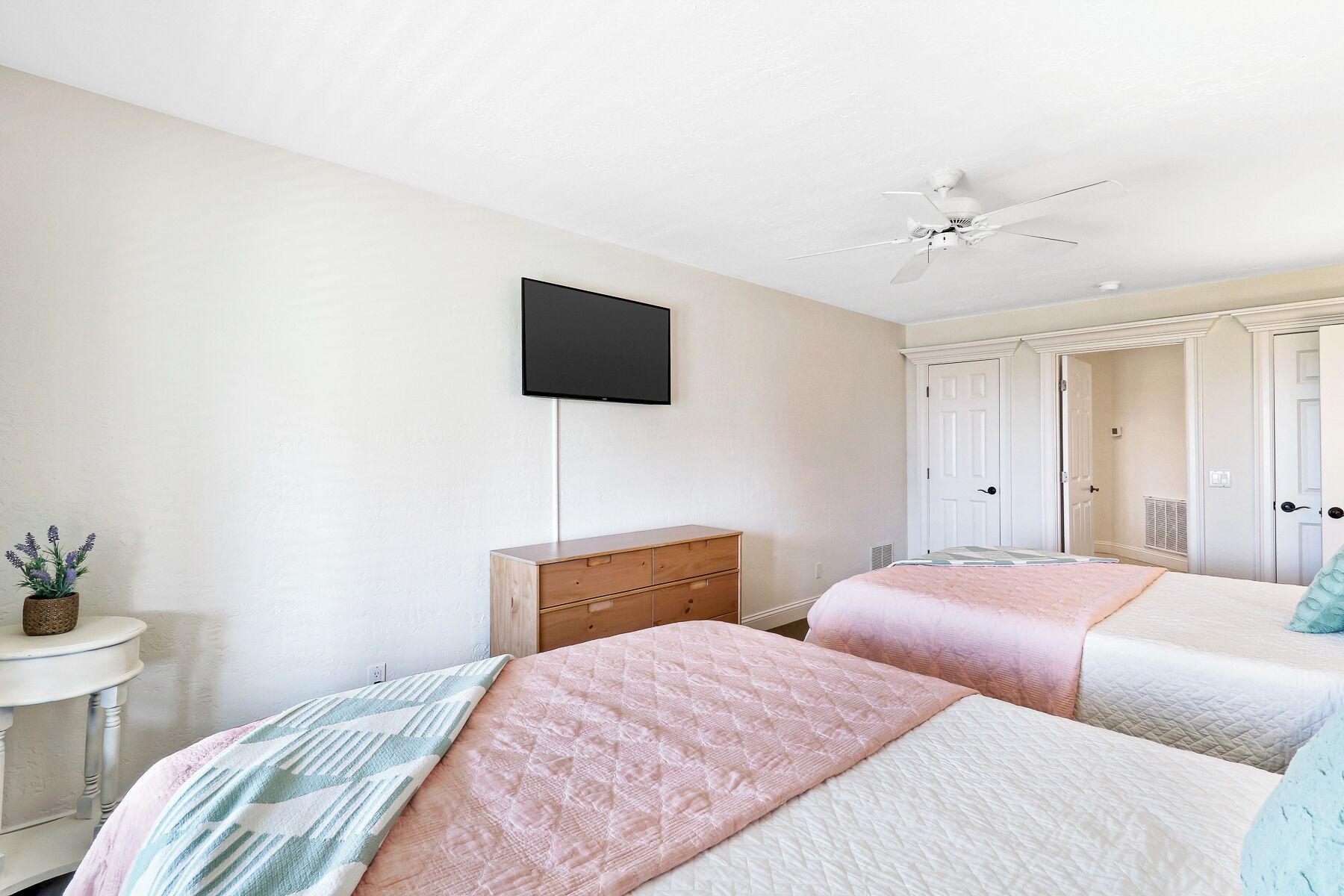 Een slaapkamer met twee bedden, een aan de muur bevestigde televisie, een plafondventilator en een dressoir.