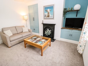 A living room with a beige sofa, a coffee table, a fireplace, a TV, and light blue cabinets. - Sunnymede (Keighley)