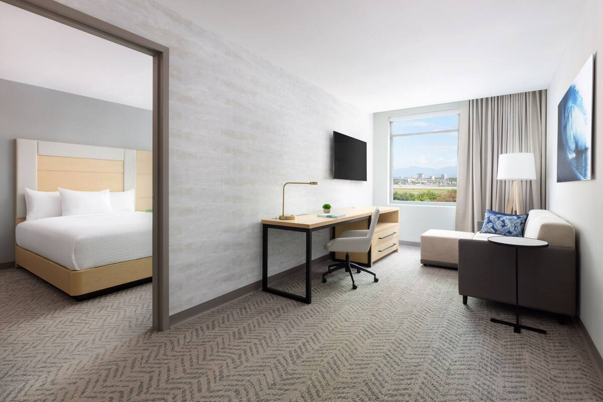Une chambre d’hôtel équipée d’un lit, d’un bureau, d’une chaise, d’un canapé et d’un téléviseur fixé au mur.