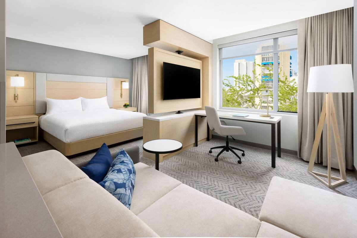 Une chambre d’hôtel moderne équipée d’un lit, d’un bureau, d’une télévision et d’un canapé.