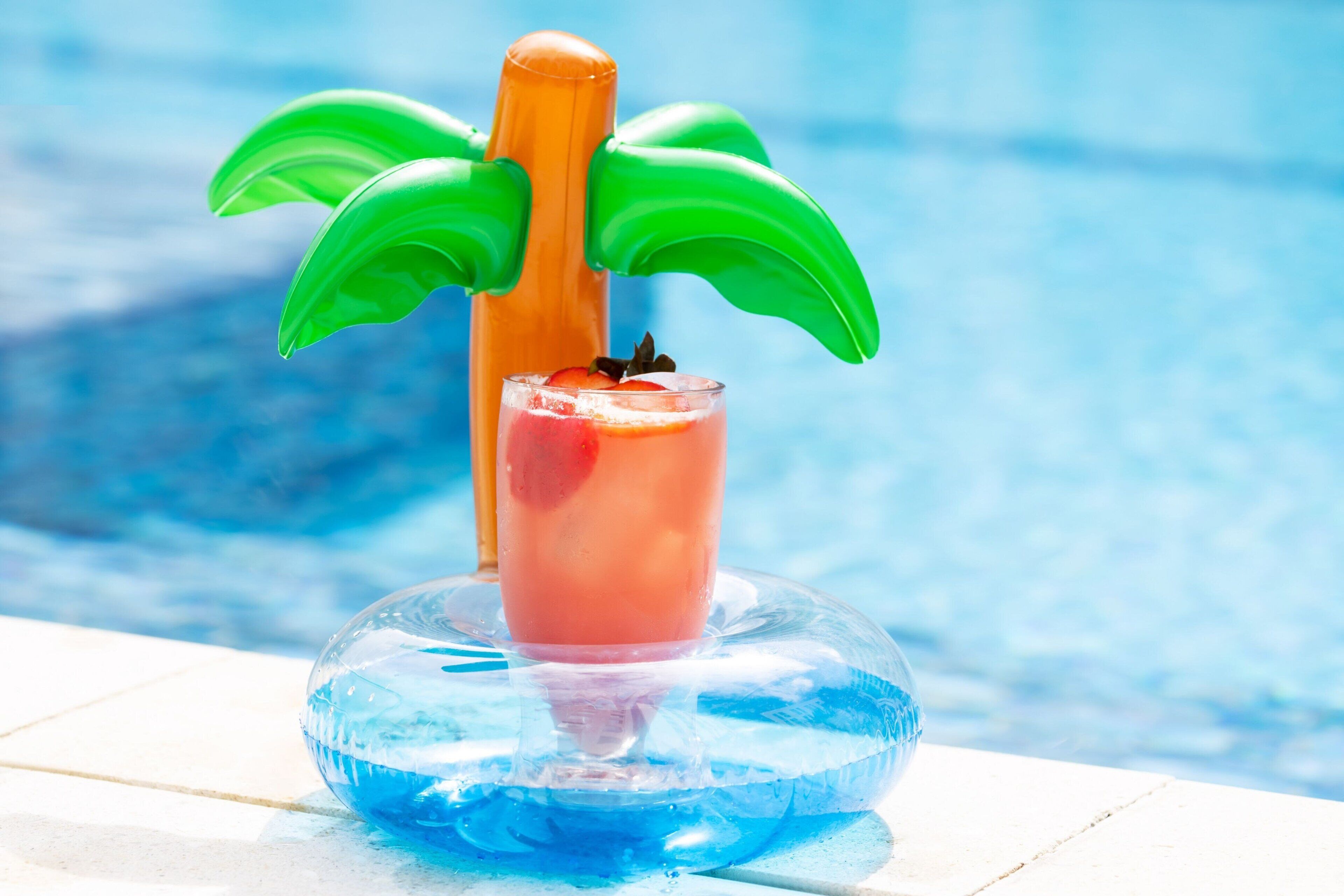 En miljö vid poolkanten med en genomskinlig glasskål som innehåller en drink och en dekorativ detalj som liknar ett palmträd.