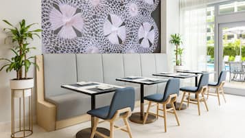 Un restaurante moderno con un banco acolchado gris, sillas de madera y un gran elemento decorativo en la pared.