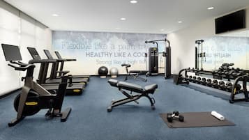 Academia moderna com equipamentos de cardio, pesos livres e uma parede com mensagens motivacionais.