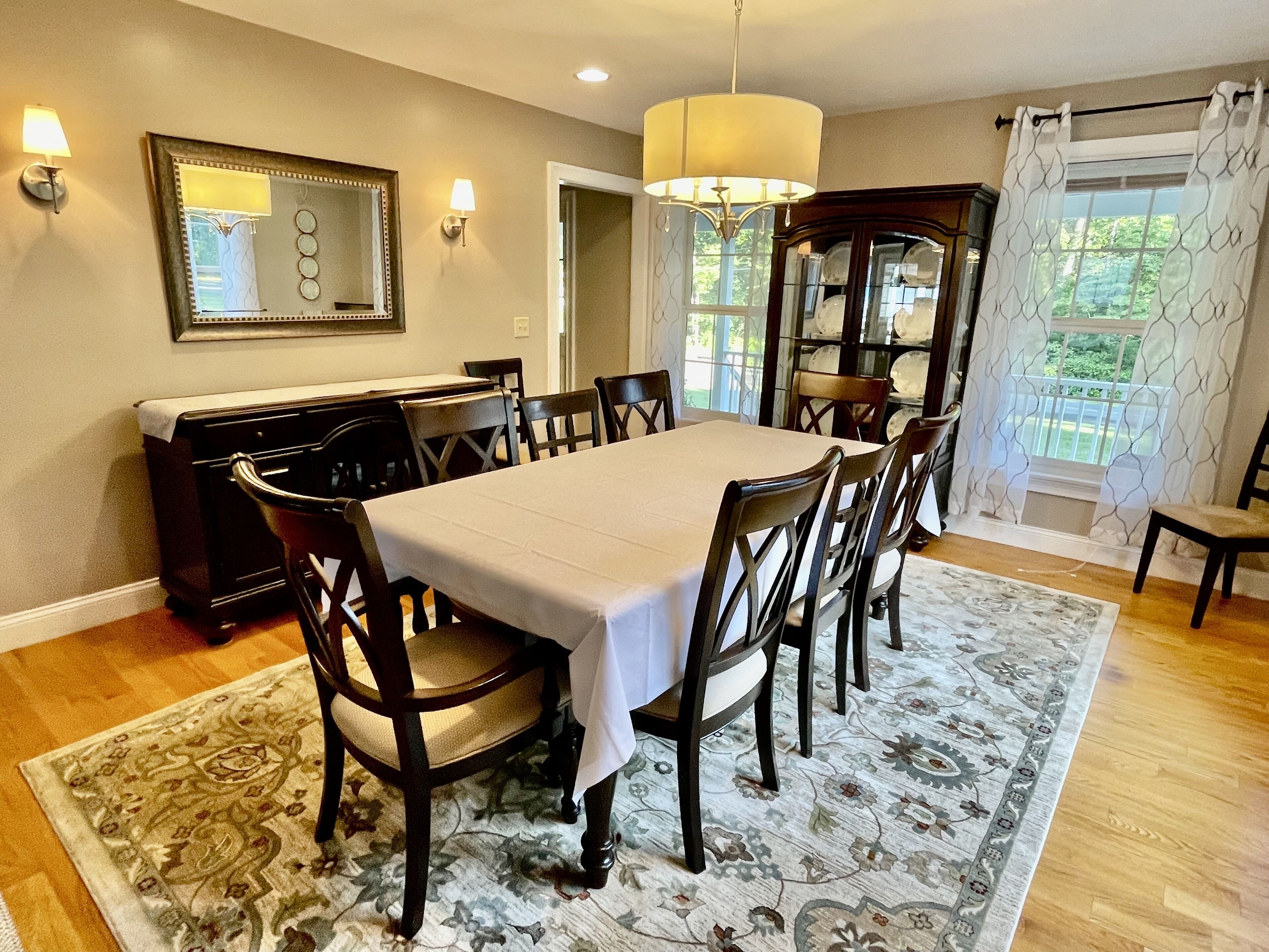 Une salle à manger avec une grande table, des chaises, un lustre et un buffet aux portes vitrées.