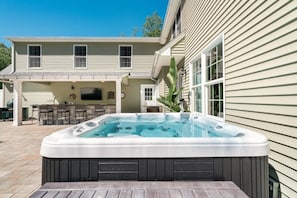 Un patio trasero con jacuzzi, mobiliario exterior y un área de patio cubierta.