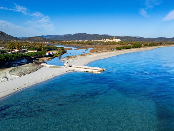 An aerial view of a coastal area with a beach, clear blue waters, and a small pier.