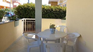 A small outdoor balcony with a round table and four chairs, a potted plant, and a view of a residential area with buildings and a hedge. - Janna e Mare Holiday Home (San Giovanni)