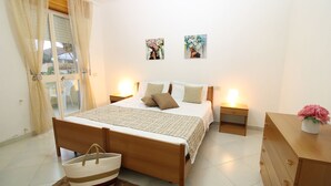 A bedroom with a wooden bed, two bedside tables with lamps, a wooden dresser, and a window with curtains. - Janna e Mare Holiday Home (San Giovanni)