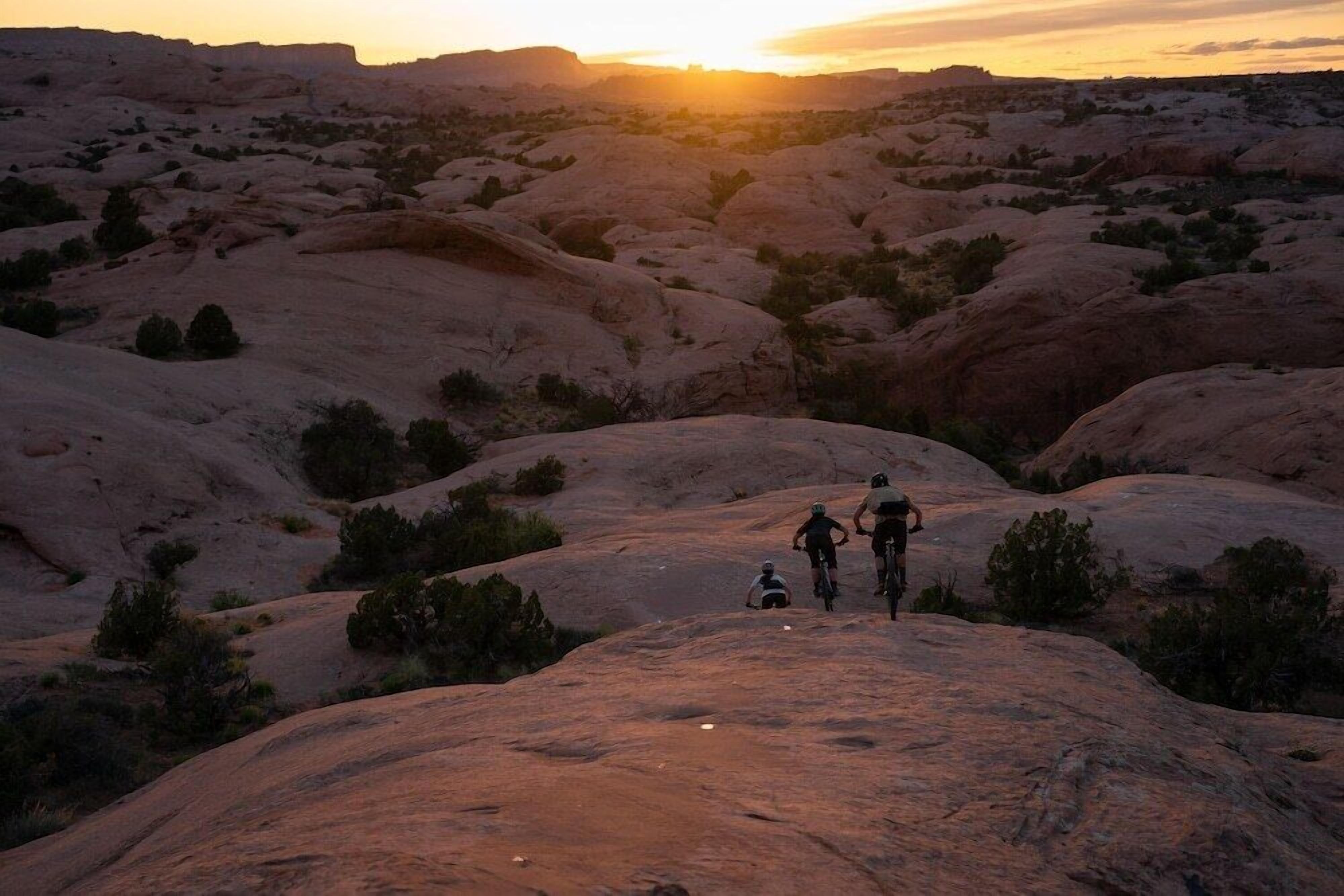 Un groupe de personnes se trouve sur un terrain rocheux, avec un coucher de soleil en arrière-plan.