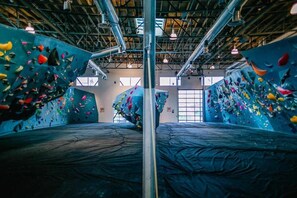 Une salle d’escalade intérieure dotée de plusieurs murs d’escalade, d’une allée centrale et d’un plafond haut avec des poutres apparentes.
