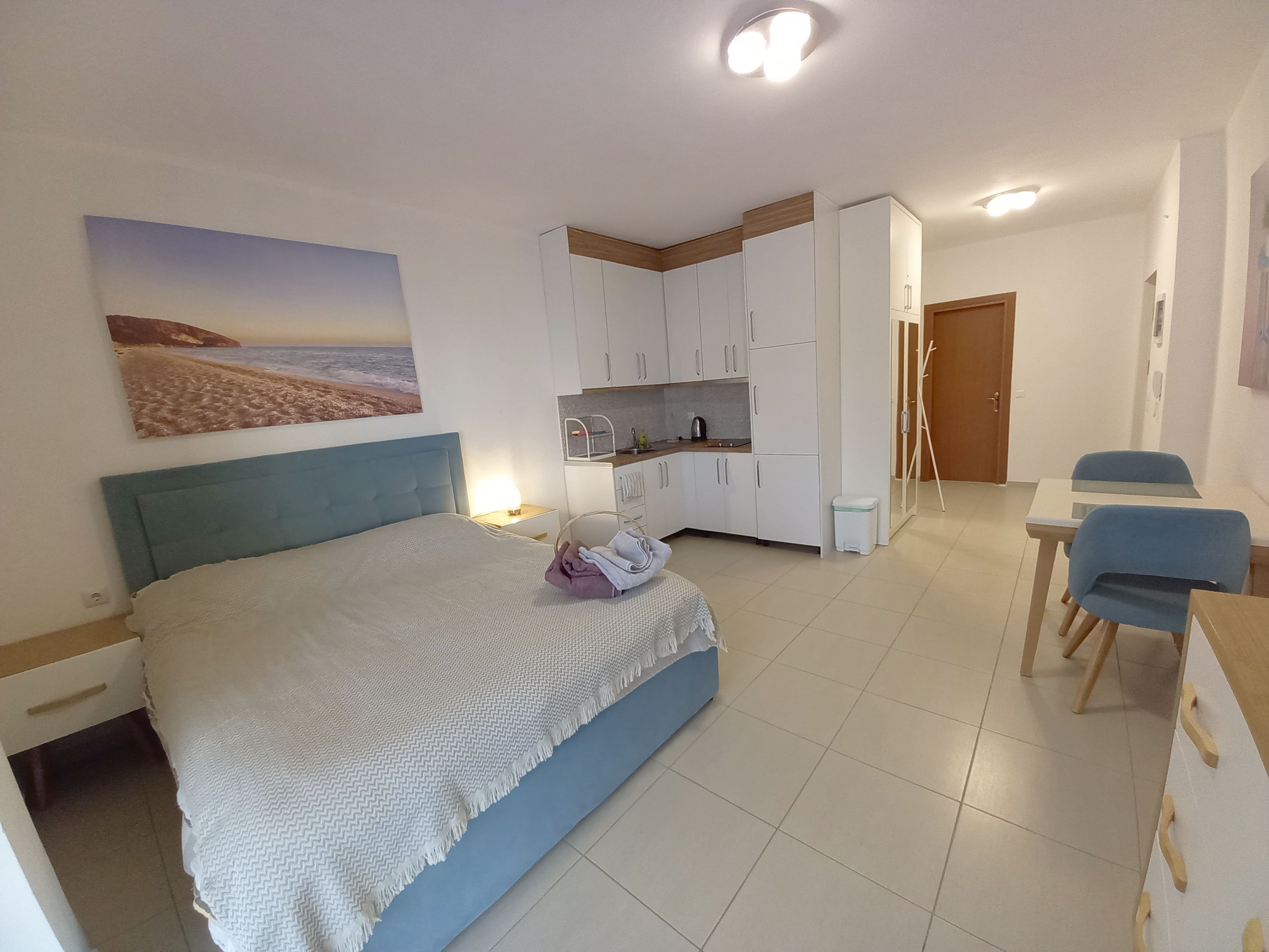 Une chambre comprenant un lit, un bureau, une chaise, un coin cuisine et une porte.