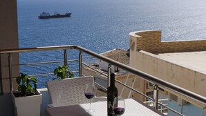 A balcony with a table and chairs, overlooking a body of water with a ship in the distance. - Modern, stylish apt by the sea with large balcony, sea view, close to the center (Sarandë)