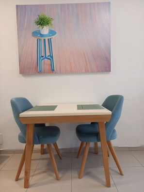 A dining table with two blue chairs, a potted plant on a blue stool, and a colorful abstract painting on the wall. - Modern, stylish apt by the sea with large balcony, sea view, close to the center (Sarandë)
