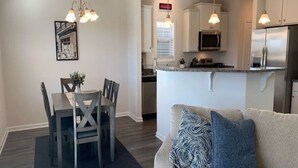 A modern kitchen with a central island, a dining area with a table and chairs, and a living room with a sofa and cushions. - New 3 Bdr Home - Clemson / Pendleton - Close to Everything (Pendleton)