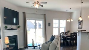 A living room with a sectional sofa, a fireplace, a flat-screen TV, and a dining area with a table and chairs. - New 3 Bdr Home - Clemson / Pendleton - Close to Everything (Pendleton)