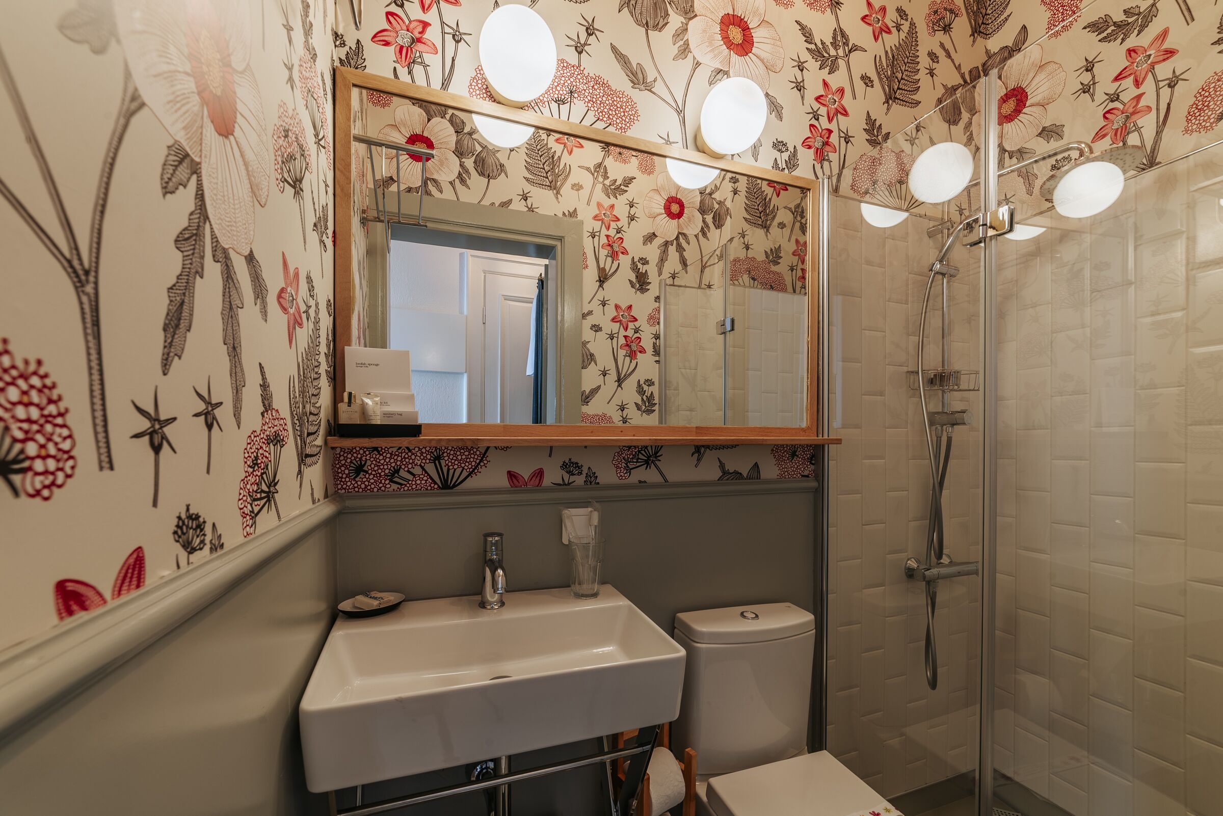 Un baño con papel tapiz floral, un lavabo, un inodoro y una ducha.