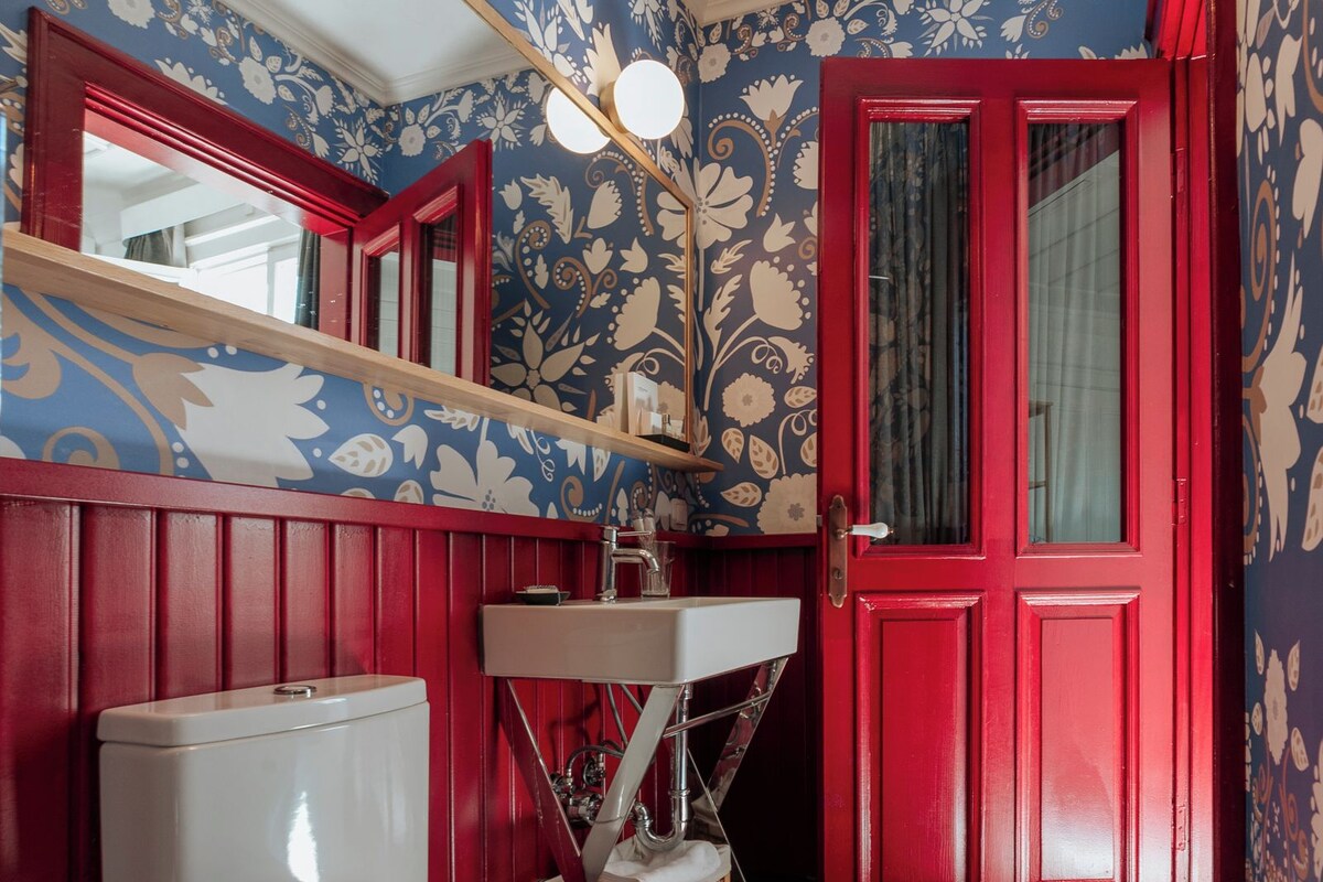Ein Badezimmer mit roter Tür, weißer Toilette und einem Spiegel über dem Waschbecken.