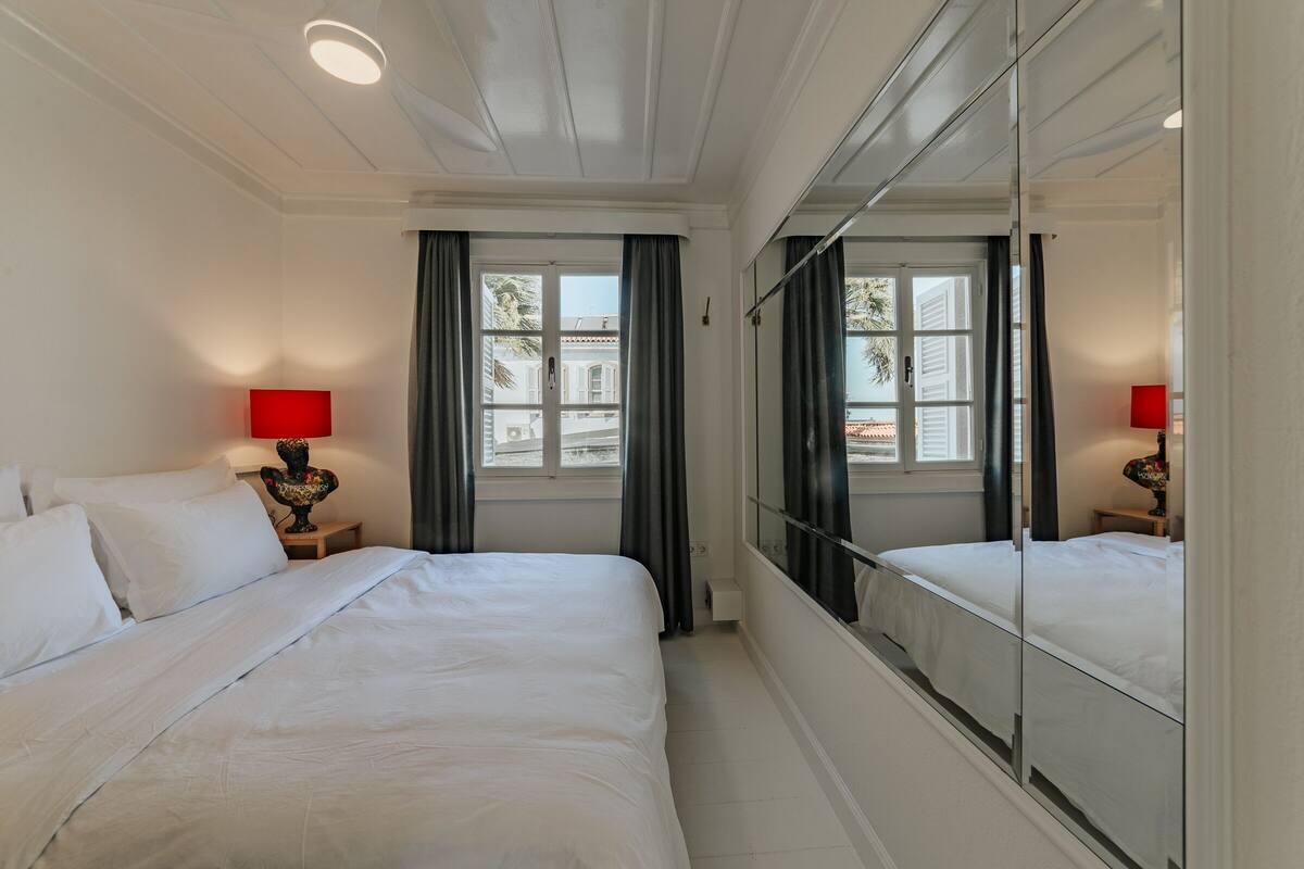 A hotel room with a large bed, two bedside tables with lamps, a large mirror, and a window with curtains.