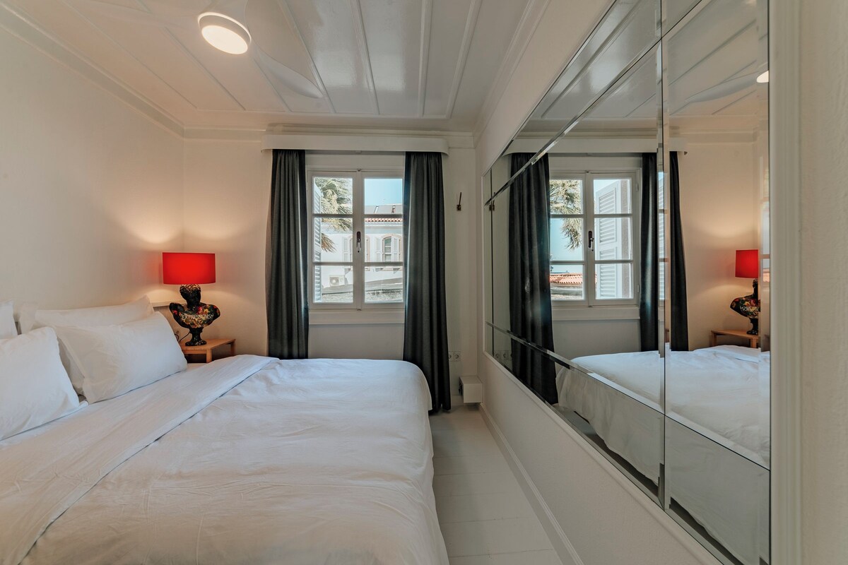 A hotel room with a large bed, two bedside tables with lamps, a large mirror, and a window with curtains.