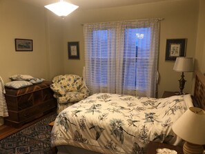 A bedroom with a bed, a chair, a nightstand, a lamp, and a dresser.