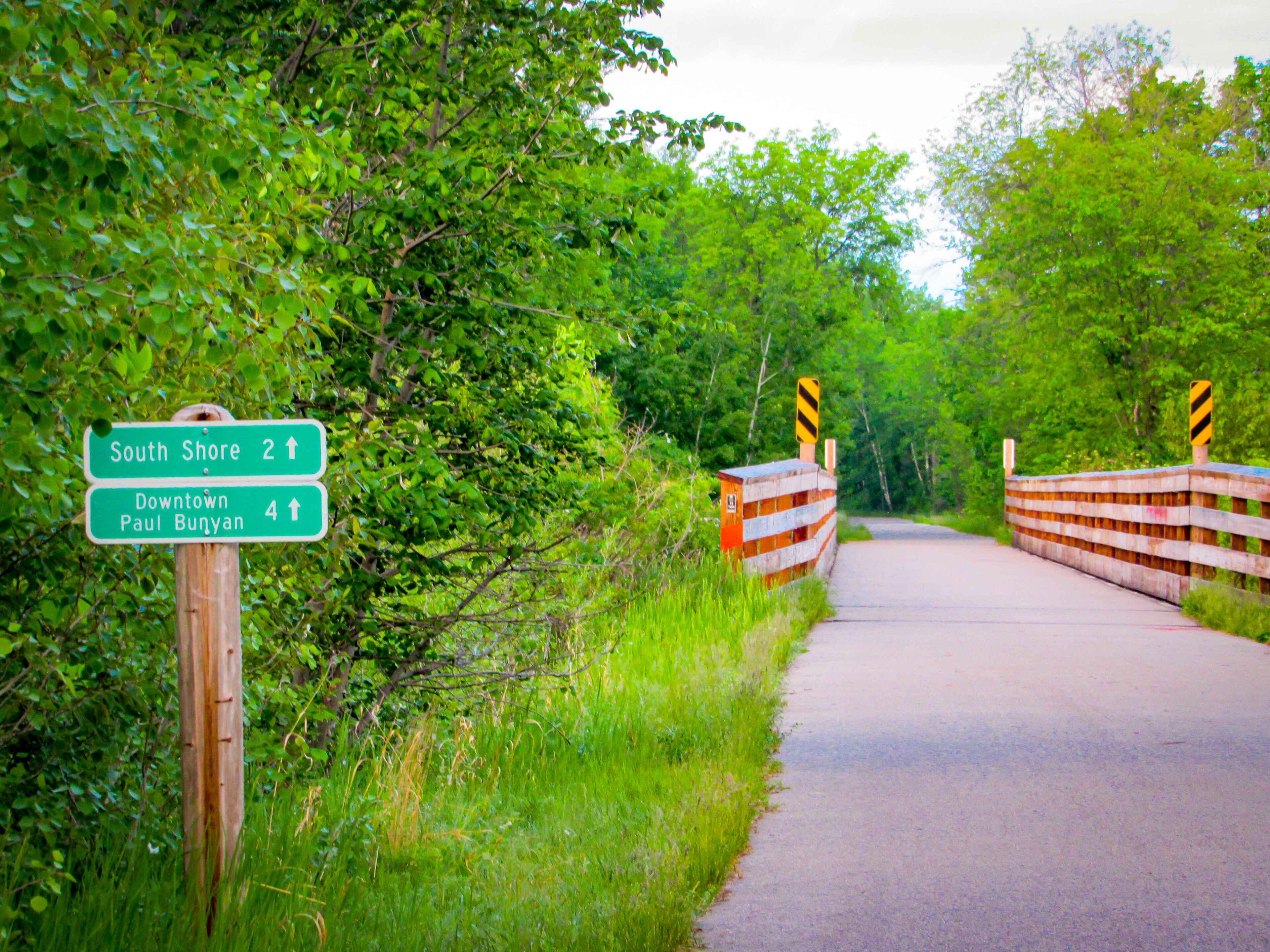 A rural road with directional signs for South Shore and Downtown Paul Bunyan.