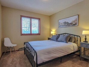 Une chambre à coucher avec un lit, une chaise, une fenêtre, une table de chevet et un tableau au mur.
