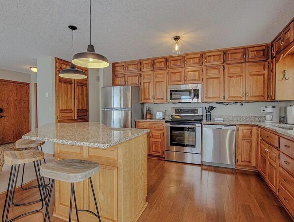 Prepare meals and socialize in this kitchen with a central island and bar stools, featuring a refrigerator, microwave, oven, and dishwasher.