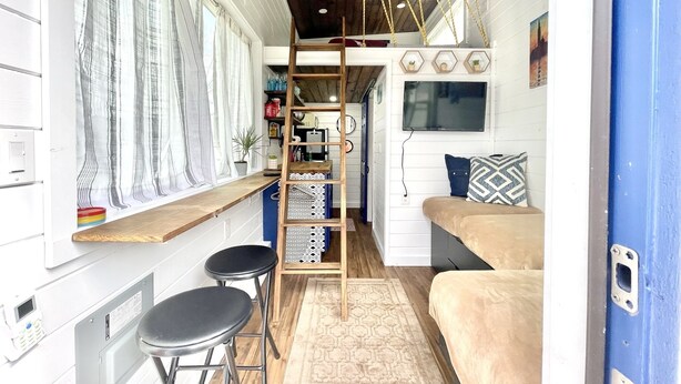 A compact, well-organized interior with a wooden ceiling, a bunk bed, a small desk with stools, and a TV mounted on the wall. - Tiny Home! With Great Layout!  Unique Stay Nurses Welcomed (Houston)