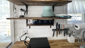 A kitchen with wooden shelves holding dishes, glasses, and utensils. There is a coffee maker, a kettle, and a knife block on the wall. - Tiny Home! With Great Layout!  Unique Stay Nurses Welcomed (Houston)