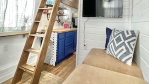 A cozy room with a wooden ladder, a TV mounted on the wall, and a sofa with a patterned pillow. - Tiny Home! With Great Layout!  Unique Stay Nurses Welcomed (Houston)