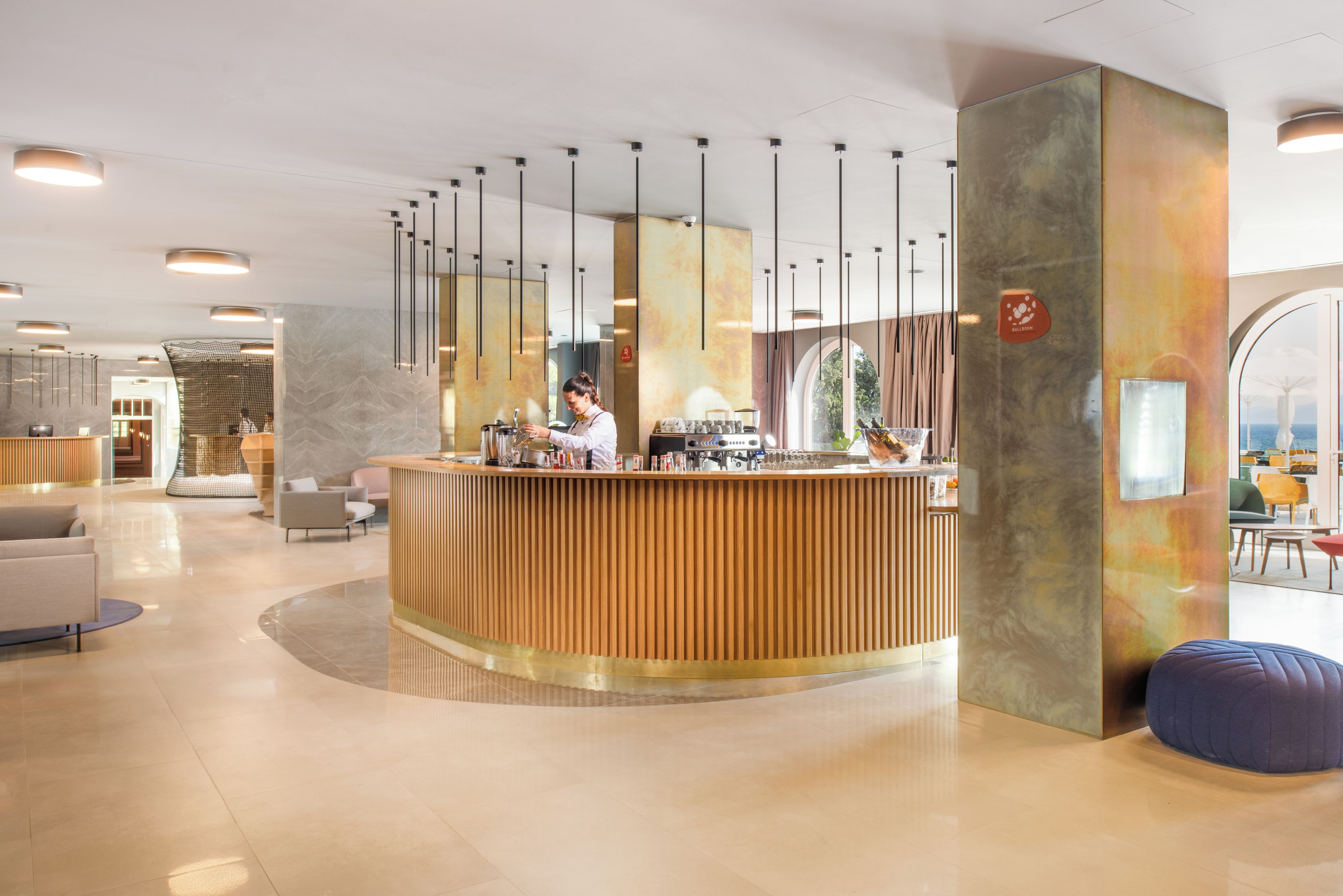 A reception area with a wooden counter, a barista preparing a drink, and a view of the sea through a large window.